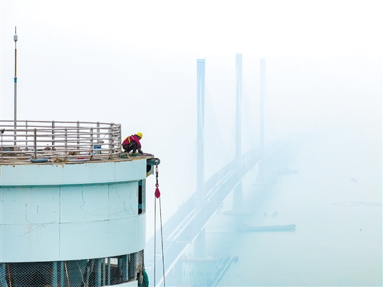 建設(shè)者在塔柱上施工，遠(yuǎn)處“海上長龍”若隱若現(xiàn)。