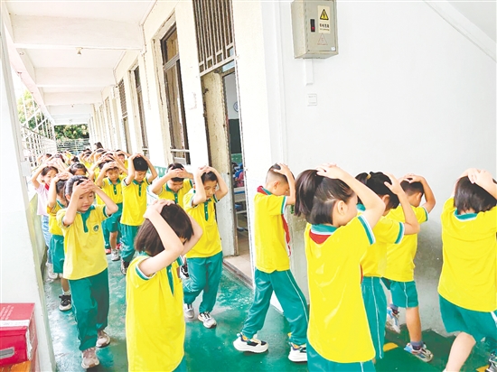 演練中，學(xué)生雙手抱頭、緊貼墻角，按照指定的逃生路線快速有序地撤離至操場安全區(qū)域。