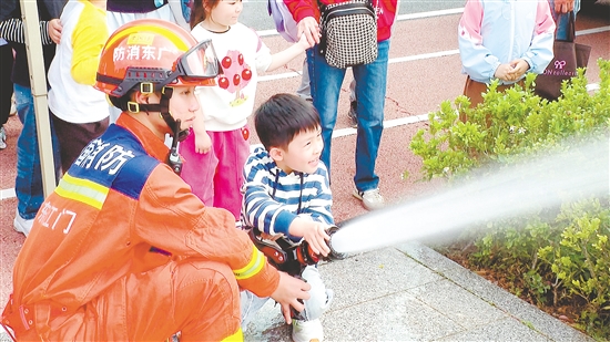 在消防員的指導(dǎo)下，小朋友體驗(yàn)使用消防水槍。